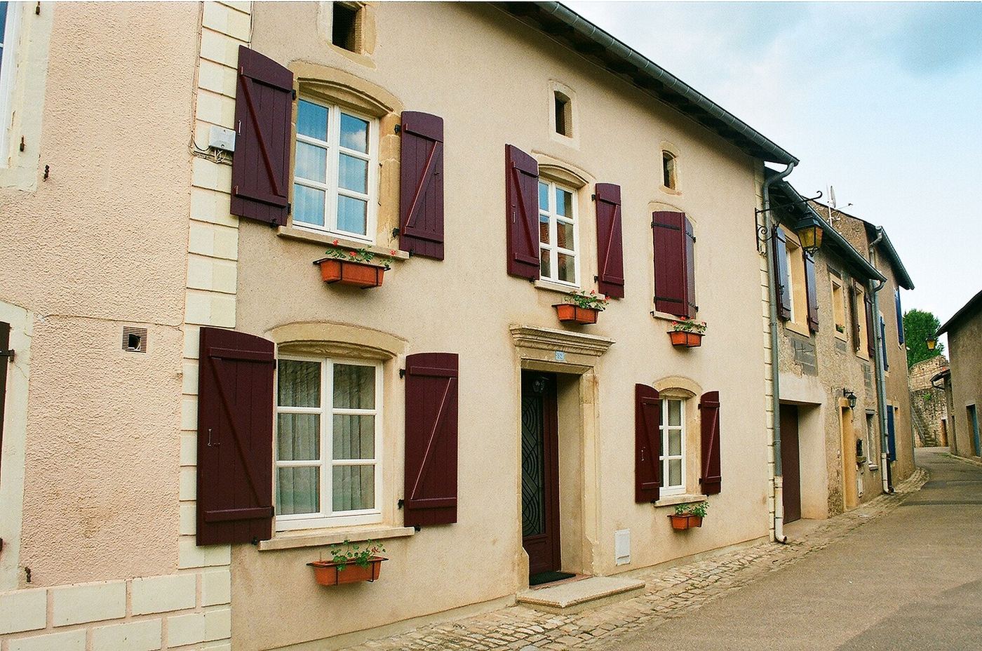 Façade en pierre à volets bois et fenêtres à petits carreaux, sur une rue montante