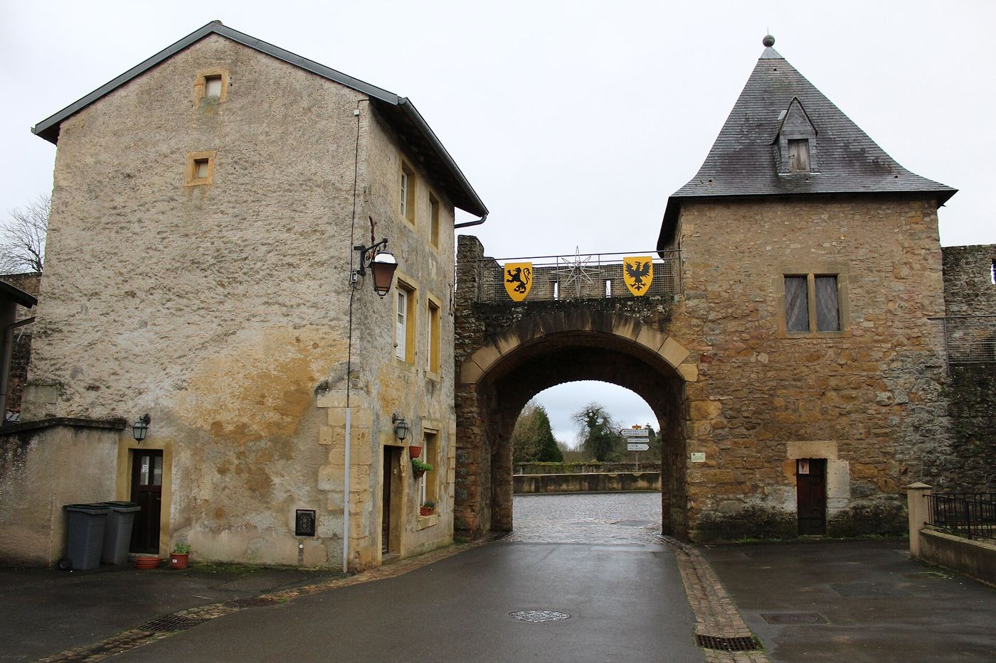 Porte fortifiée en pierre, son arche et la maison de l'octroi, au bout de la rue